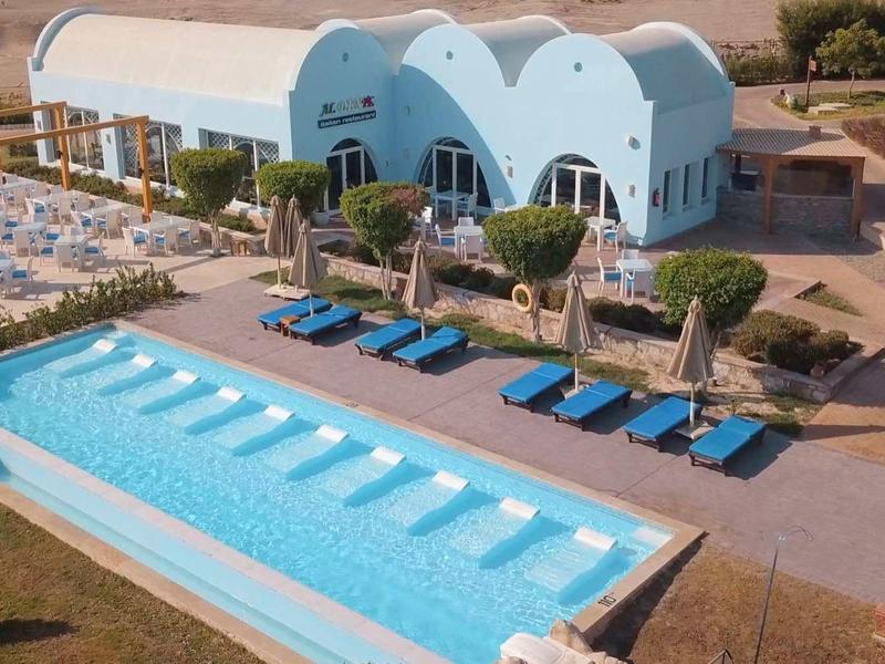 Modern pool area with loungers and umbrellas in front of light blue hotel building.