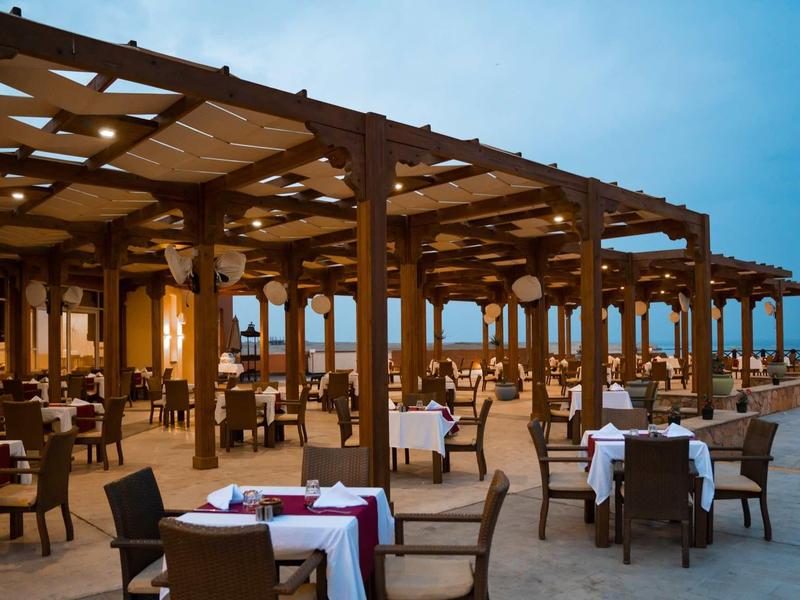 Open-air restaurant with wooden beams and set tables at sunset.