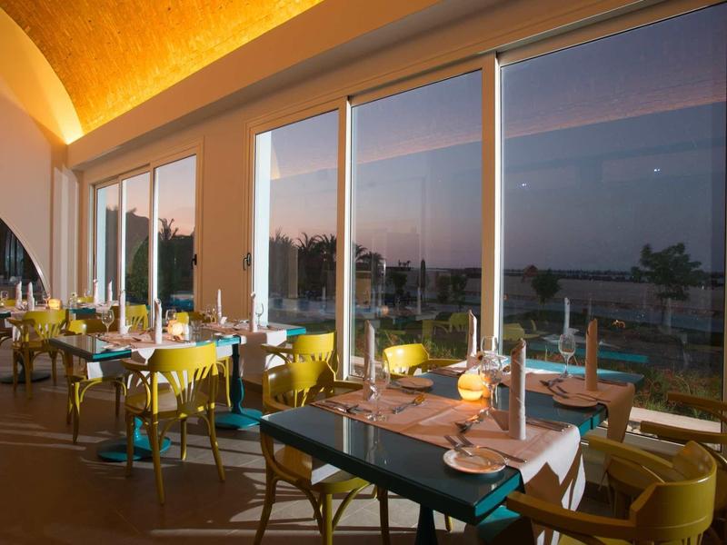 Elegant restaurant with large windows and yellow lighting at sunset.