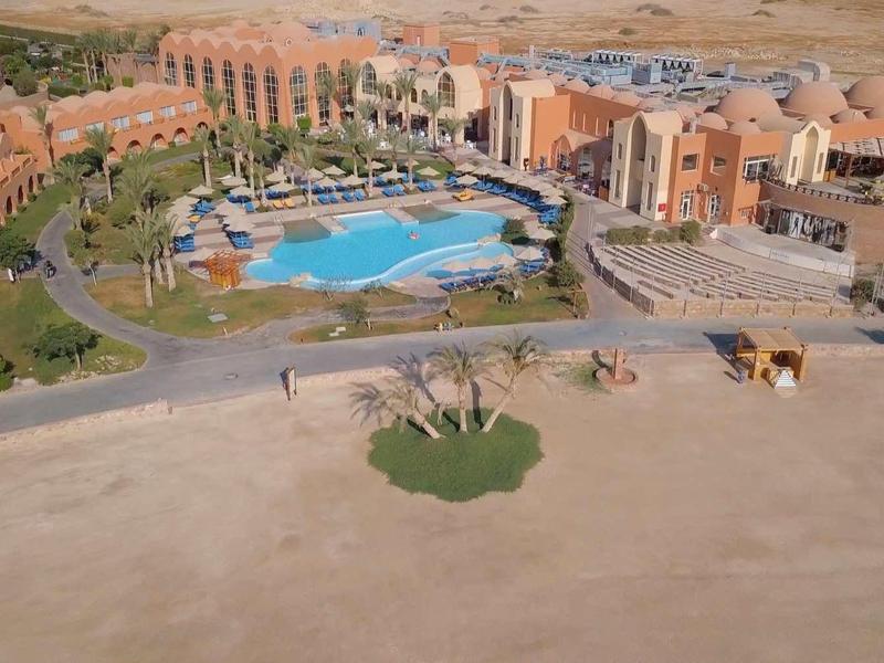 Large resort with multiple buildings and a large pool in a desert-like setting.