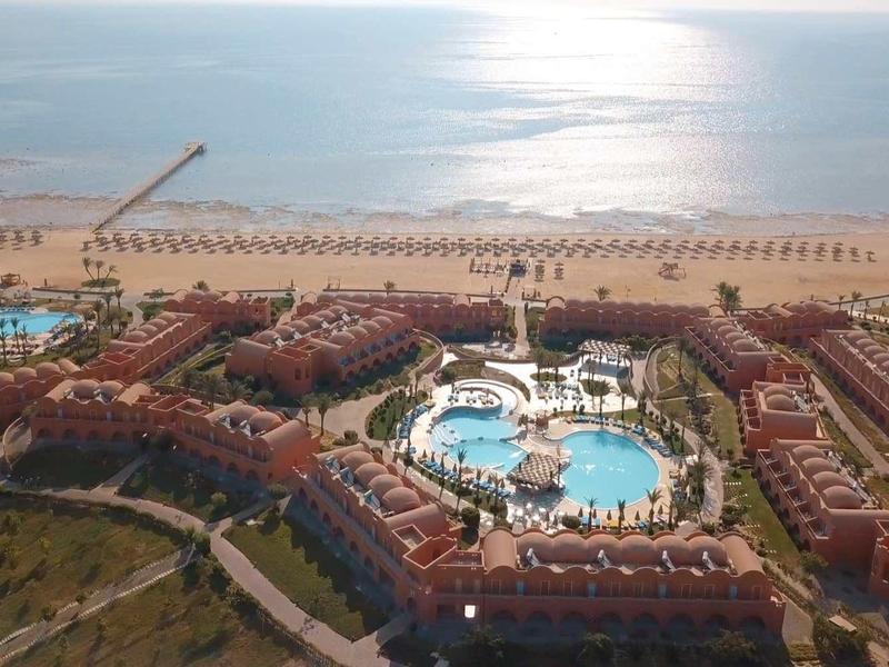 Aerial view of a large holiday resort with pools and direct beach access at sunset.