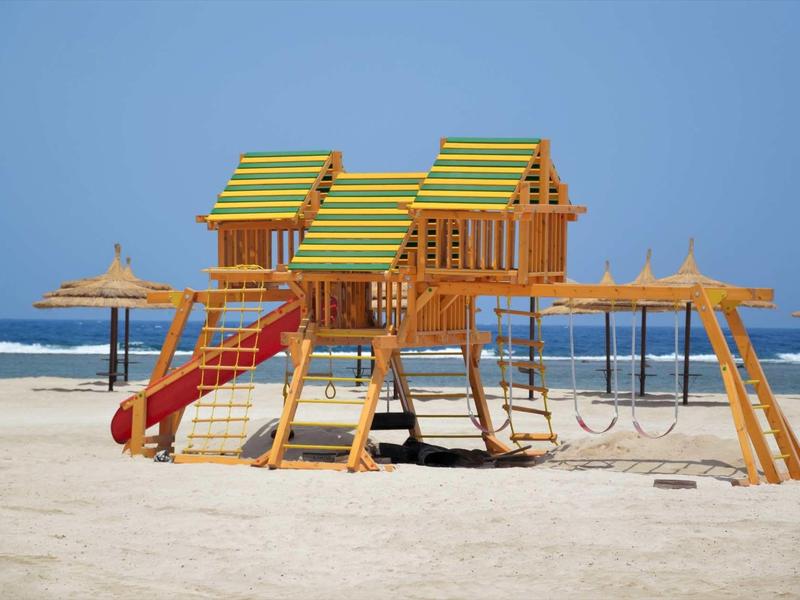 Colorful children's playground with slides and swings on the beach under clear sky.