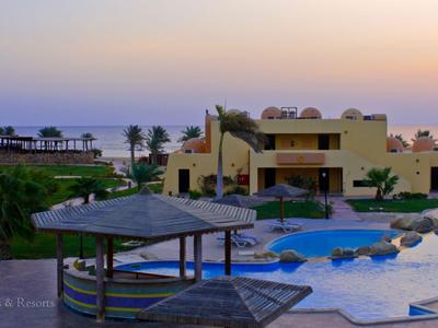 Blick auf einen Hotelpool mit Sonnenschirmen und Gebäuden bei Sonnenuntergang