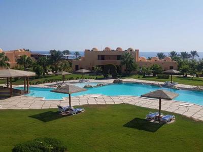 Großer Außenpool mit Sonnenschirmen und Liegen auf gepflegtem Rasen vor Hotelgebäuden.