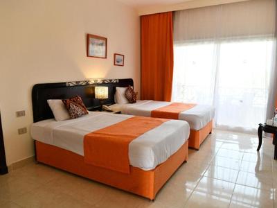 Chambre d'hôtel lumineuse avec deux lits simples et rideaux orange.