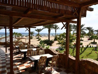 Überdachte Terrasse mit Tischen und Stühlen bietet Blick auf Garten und Strand