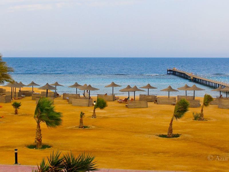 Plage avec parasols et palmiers, sable jaune et mer bleue calme.