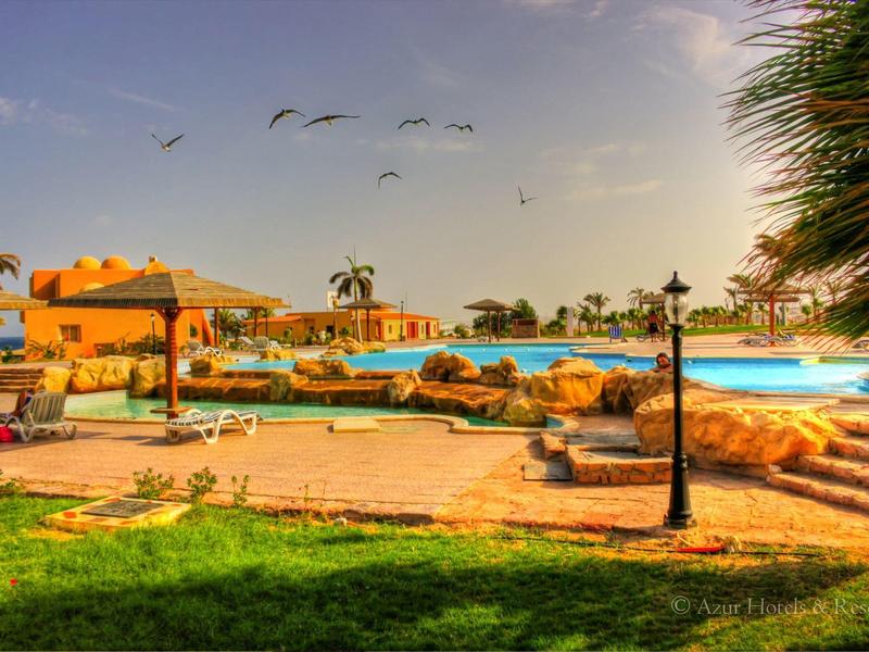 Piscine extérieure dans un complexe hôtelier avec parasols et pelouse verte.