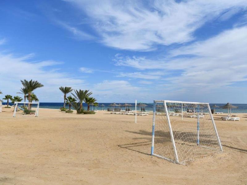 Terrain de football sur une plage sablonneuse avec vue sur mer et ciel partiellement nuageux.