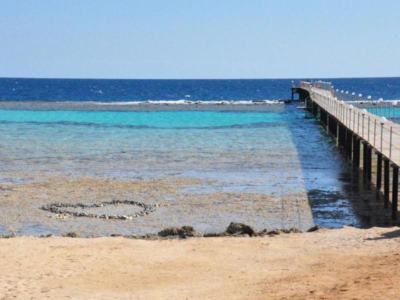 Plage avec sable, eau turquoise, ponton en bois s'étendant sur la mer calme.