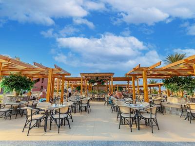 Außenbereich eines Hotels mit Tischen und Stühlen unter Holzpergolen bei sonnigem Himmel.