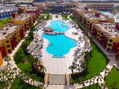 Großer Hotelpool mit vielen Liegestühlen und bunten Gebäuden ringsum.