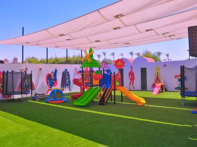 Spielplatz mit bunter Rutsche und Schaukeln unter einem Sonnensegel auf grünem Kunstrasen