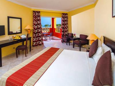 Helles Hotelzimmer mit Doppelbett, Schreibtisch und großem Fenster zur Terrasse mit Meerblick.