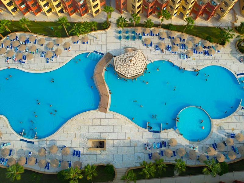 Außenpool mit mehreren Bereichen und Sonnenschirmen neben einem Hotelgebäude.