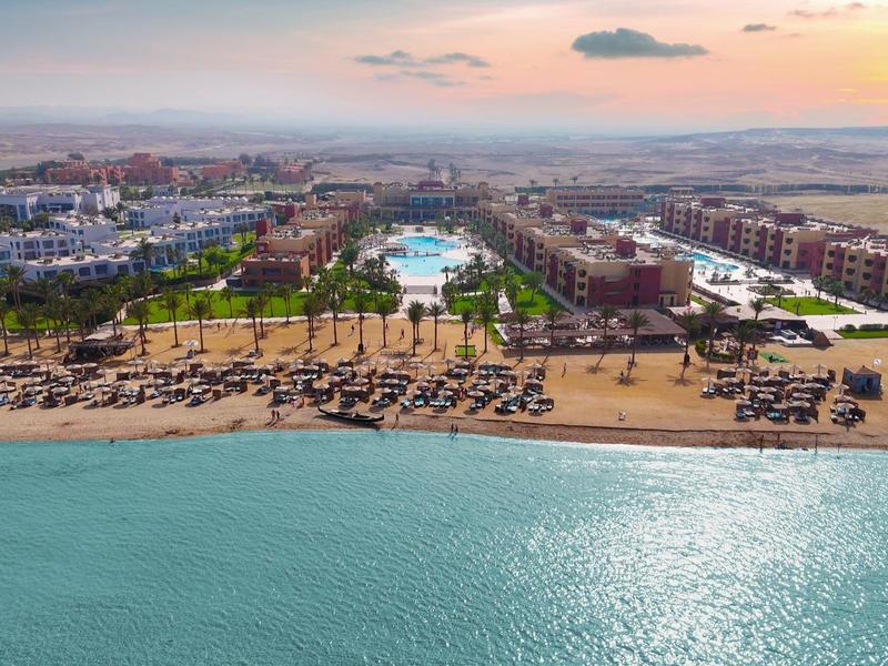 Strandresort mit Pools, Palmen und Liegestühlen entlang des Sandstrands am ruhigen Meer.