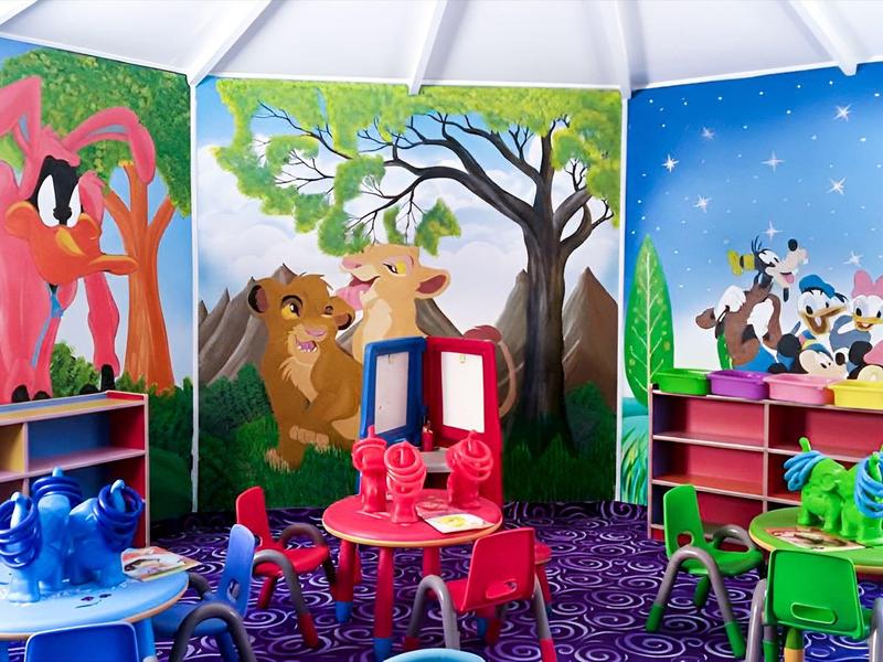 Buntes Kinderspielzimmer mit Tiermotiven, kleinen Tischen und Stühlen, Regalen und Wandmalereien.
