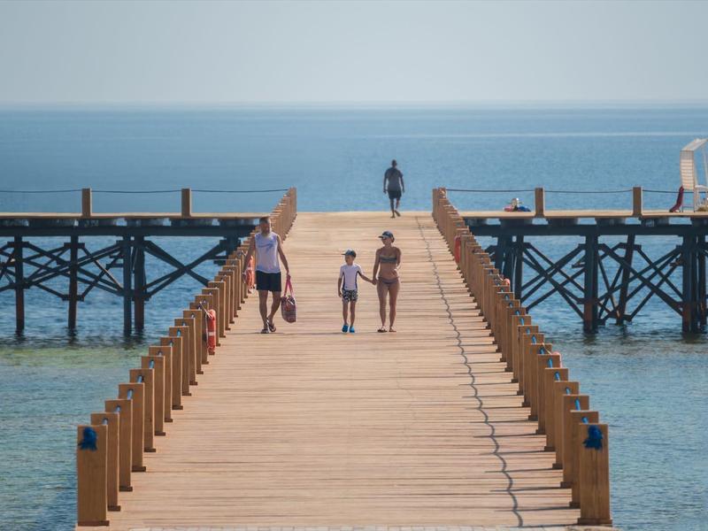 Jetée en bois s'étendant sur une mer calme avec trois personnes marchant dessus.
