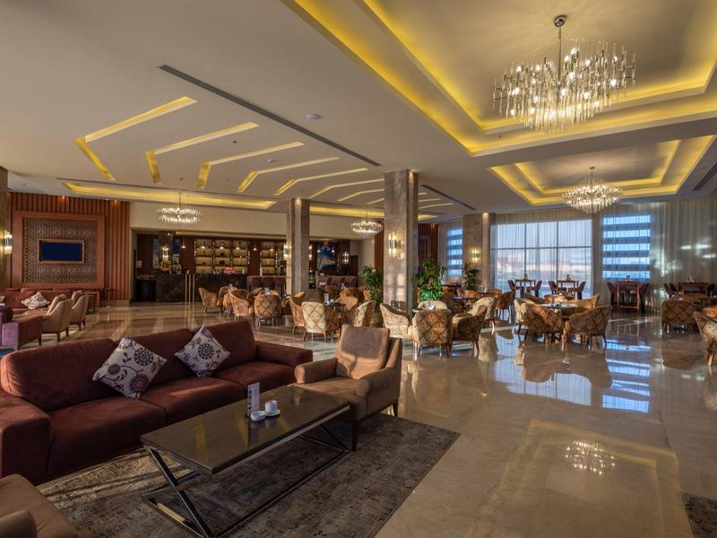 Salon d'hôtel spacieux avec canapés, tables basses, éclairage moderne et grandes fenêtres.