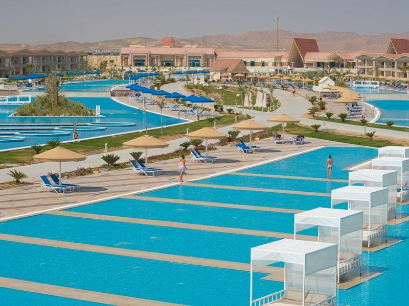 Piscines bleues avec cabines blanches entourées de transats dans un complexe hôtelier désert.