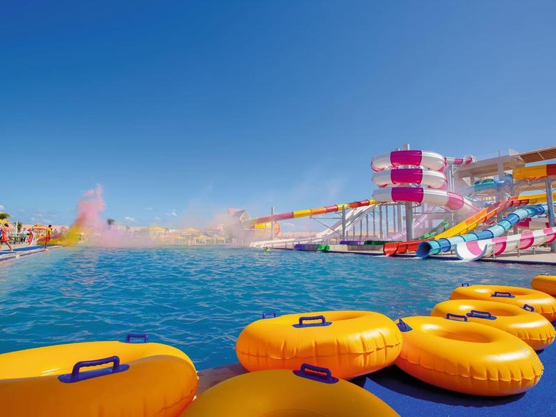 Toboggans colorés et bouées jaunes dans un parc aquatique sous un ciel bleu clair.