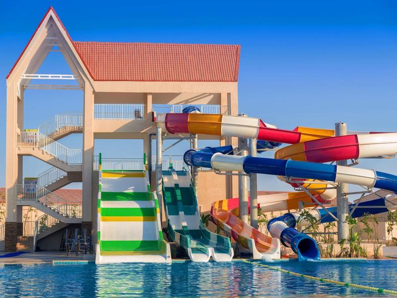 Toboggans colorés menant à une grande piscine sous un ciel bleu dégagé.