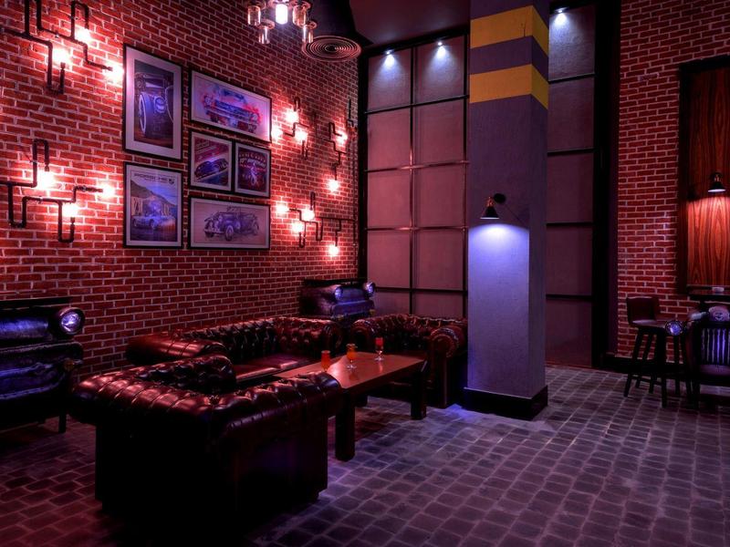 Salon d'hôtel avec éclairage tamisé, canapé en cuir noir, murs en briques rouges et tables basses.