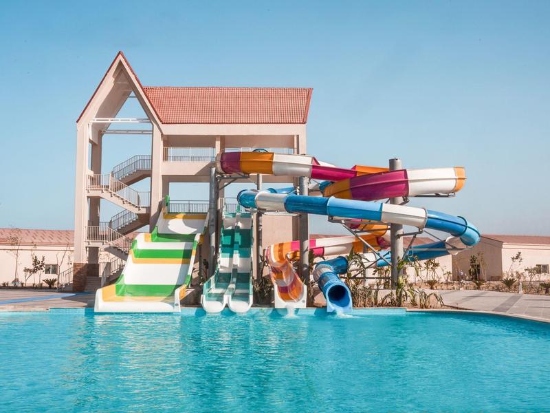 Toboggans colorés au-dessus d'une piscine d'hôtel sous un ciel bleu clair.