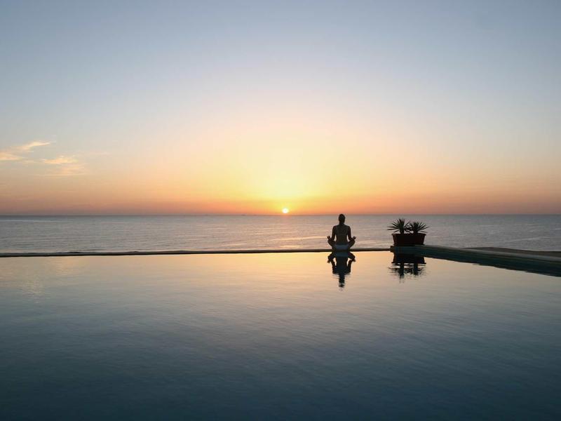 Sonnenuntergang am Meer mit zwei Personen, die am Rand eines ruhigen Pools sitzen.