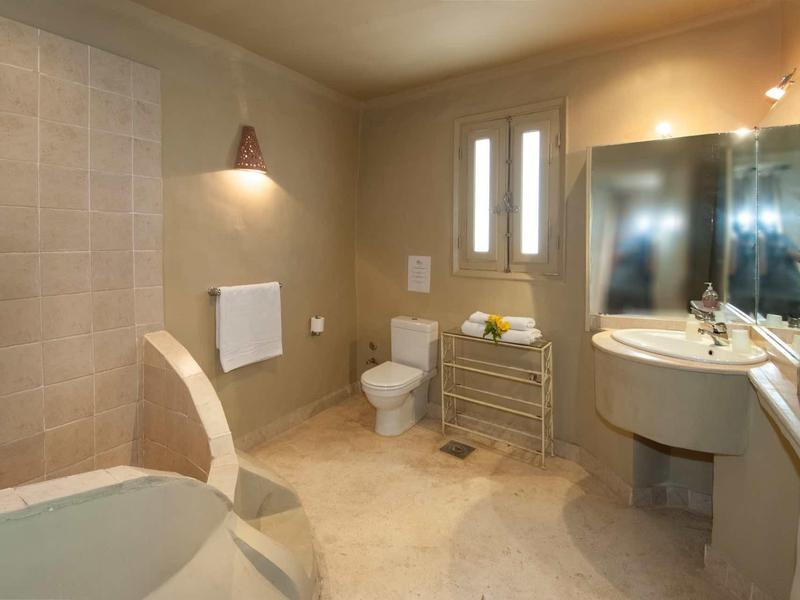 Großes Badezimmer mit beiger Fliesenwand, Sitzbadewanne, Toilette und rundem Waschbecken.