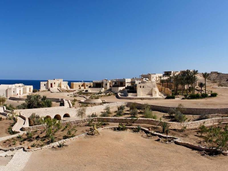 Weite Wüstenlandschaft mit antiken Ruinen und blauem Himmel im Hintergrund.