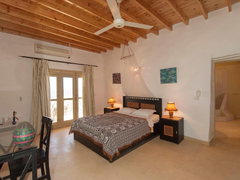 Schlafzimmer mit Holzbalkendecke, Deckenventilator, Doppelbett, Nachttischen, Schreibtisch und Lampen.