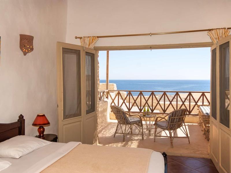 Helles Schlafzimmer mit Doppelbett und offener Balkontür, Blick auf Terrasse und Meer.
