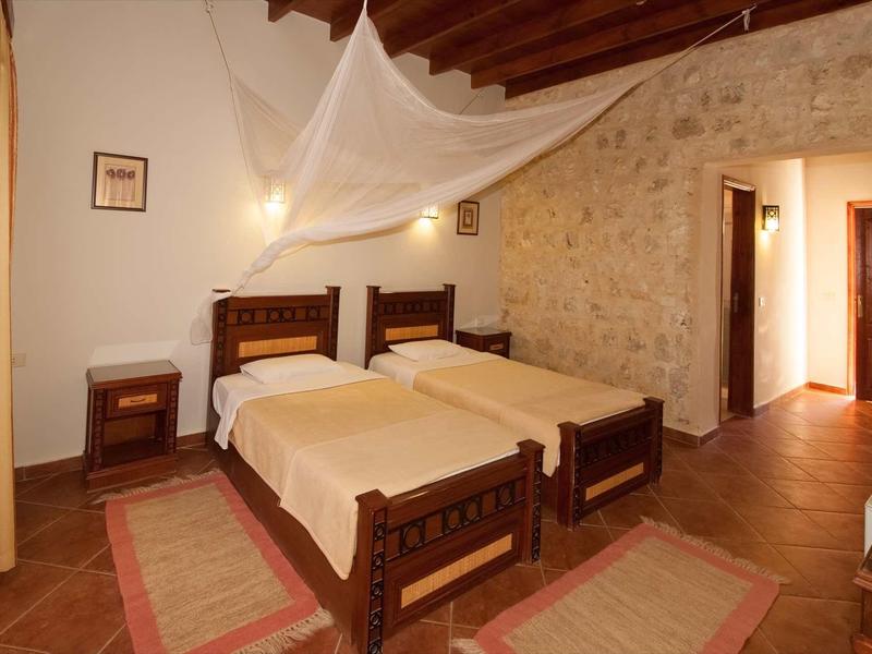 Einfaches Schlafzimmer mit zwei Einzelbetten, Holzdecke und Steinwand im warmen Licht.