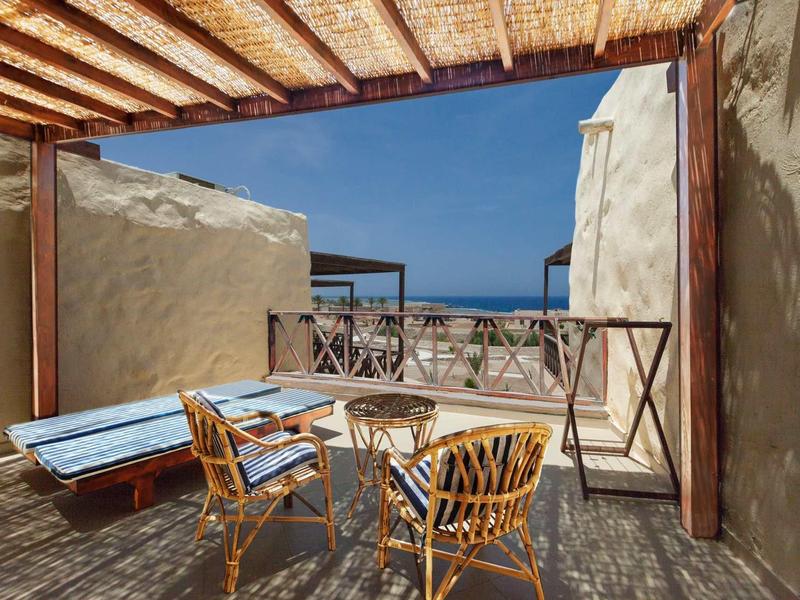 Terrassenbereich mit Bambusstühlen, Tisch, Liegestuhl, Steinwänden und Blick auf das blaue Meer.