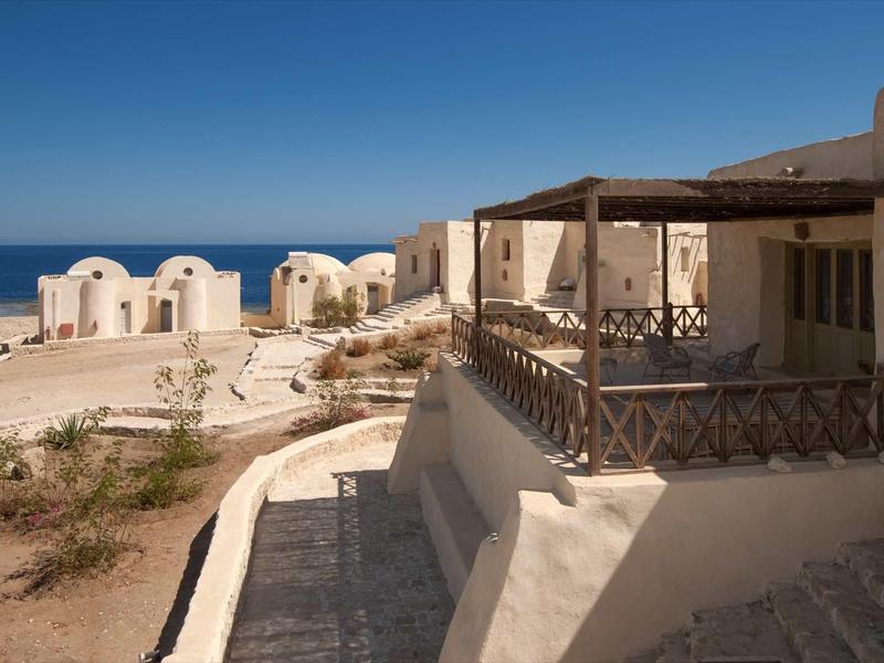 Weiße Häuser mit Runddächern und Terrasse am Strand unter klarem blauem Himmel.