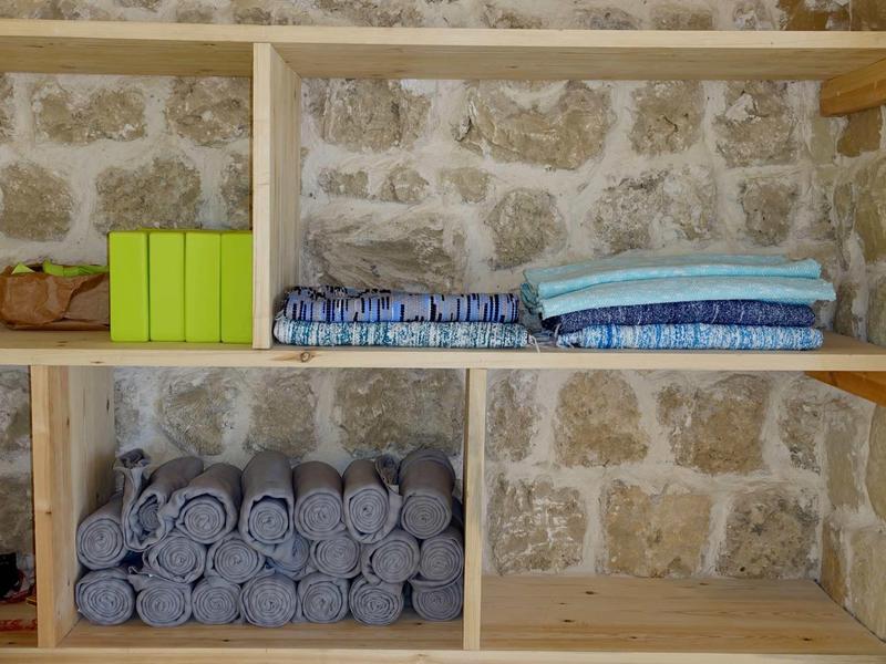 Holzregal vor Steinwand mit grünen Büchern, gefalteten Decken und grauen Handtüchern.