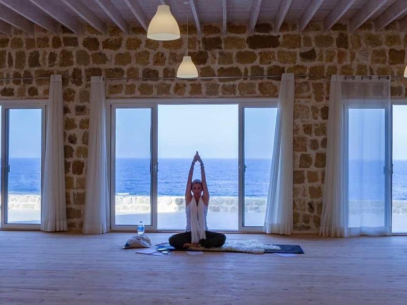 Großer Raum mit Steinwänden, drei breiten Fenstern und Blick auf das Meer bei Tageslicht.