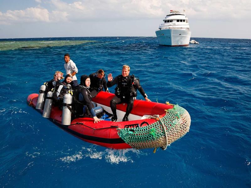 Mehrere Taucher in einem roten Schlauchboot auf blauem Meer, im Hintergrund ein weißes Schiff.