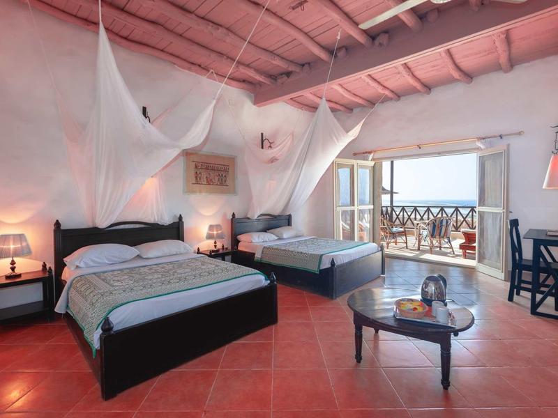 Ein Zimmer mit zwei Doppelbetten, Moskitonetzen, roten Fliesen und Balkon mit Meerblick.