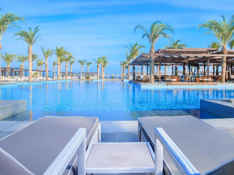 Piscine à débordement avec transats et palmiers dans un cadre de vacances ensoleillé.