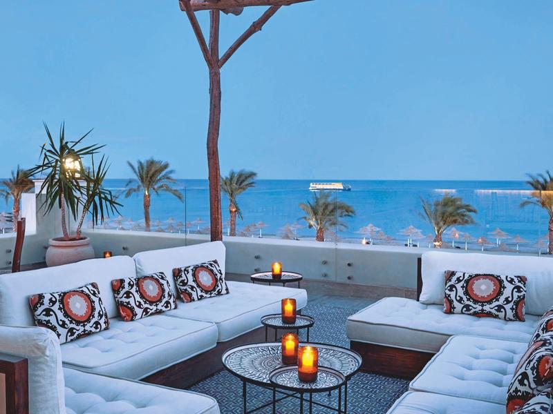 Terrasse cosy avec canapés blancs et vue sur la plage et la mer au coucher du soleil.