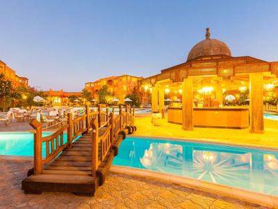 Großer Außenpool mit Holzbrücke und beleuchtetem Pavillon in warmem Abendlicht.
