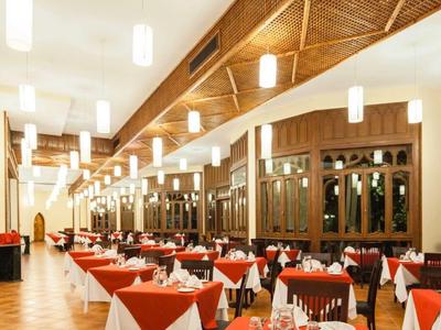 Großer Speisesaal mit rot-weißen Tischdecken, vielen gedeckten Tischen und Holzdecke mit Lampen.