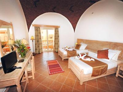 Geräumiges Schlafzimmer mit Balkon, Holzmöbeln, Fliesenboden und warmen Erdtönen.