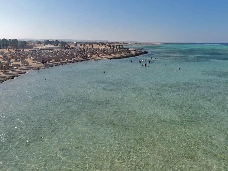 Klarer, flacher Strand mit vielen Sonnenschirmen und Liegestühlen entlang der Küste bei sonnigem Wetter.
