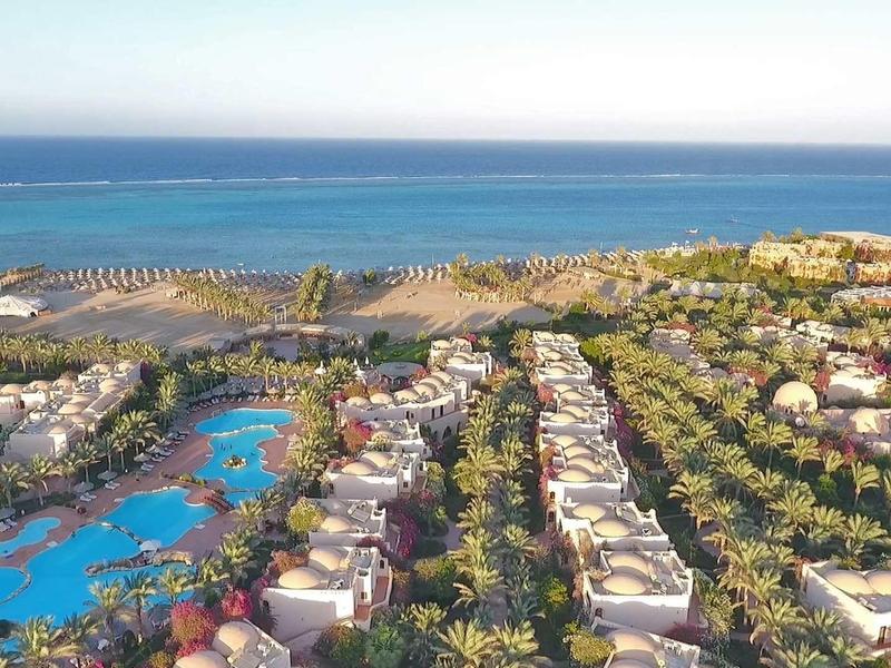 Große Hotelanlage mit blauen Pools, Palmen und Gebäuden nahe dem blauen Meer und Strand.