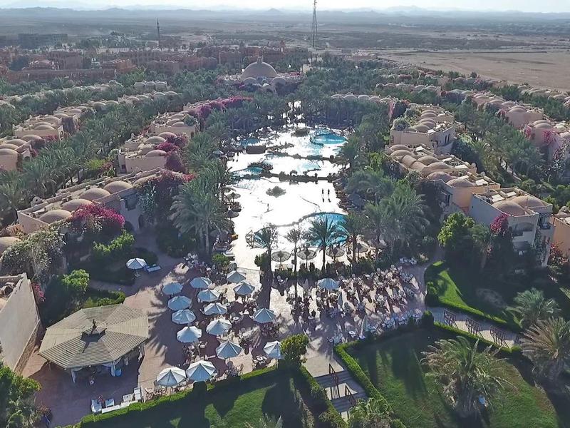 Luftaufnahme einer Wohnsiedlung mit Reihenhäusern und einem zentralen Bereich mit Pools und Sonnenschirmen.