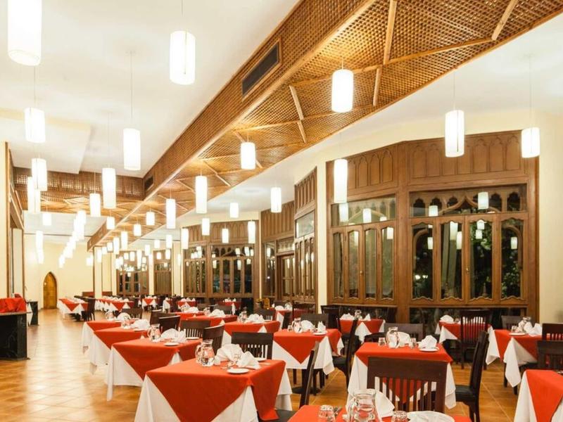 Großer Speisesaal mit rot-weißen Tischdecken, vielen gedeckten Tischen und Holzdecke mit Lampen.