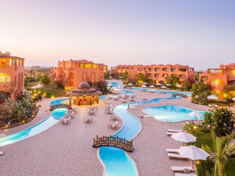 Große Hotelanlage mit mehreren Poolbereichen, Liegestühlen und mediterranen Gebäuden bei Sonnenuntergang.